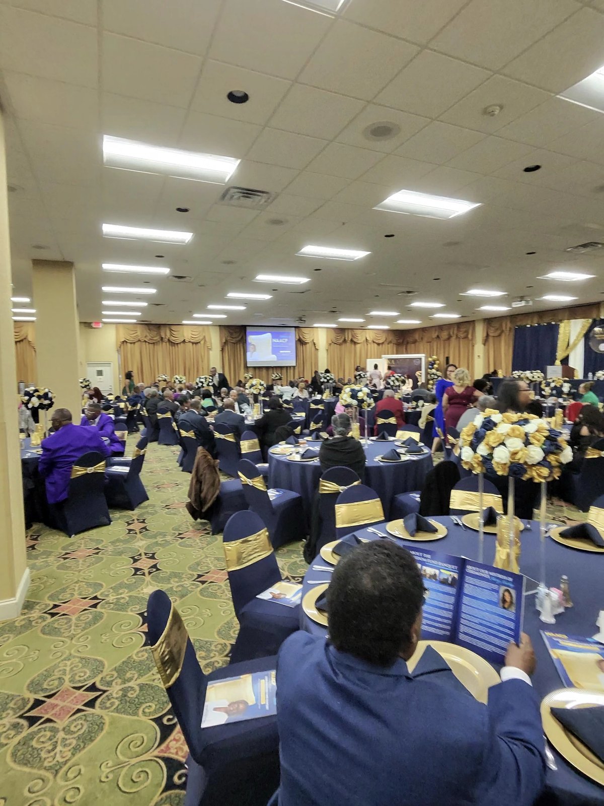 The Whispering Woods ballroom set with navy and gold tables filling in before the banquet program