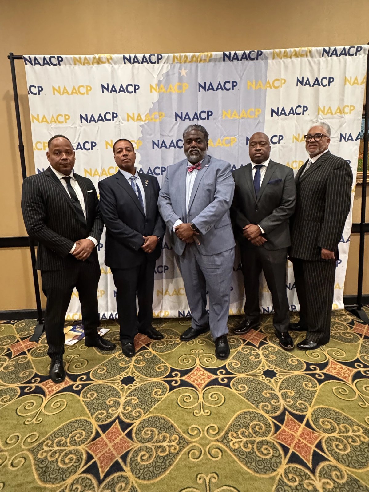 Five men in suits standing in front of a white NAACP step-and-repeat banner at the banquet
