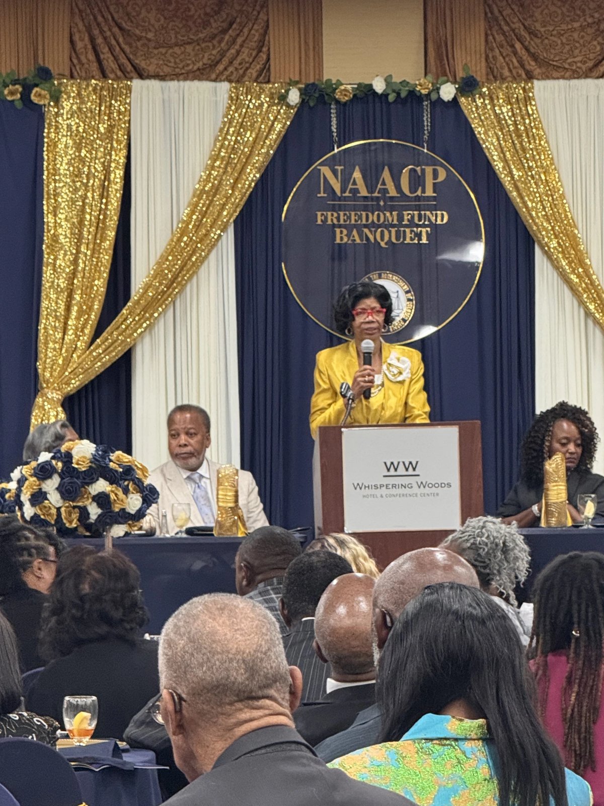 Speaker at the podium in front of the NAACP Freedom Fund Banquet backdrop at Whispering Woods